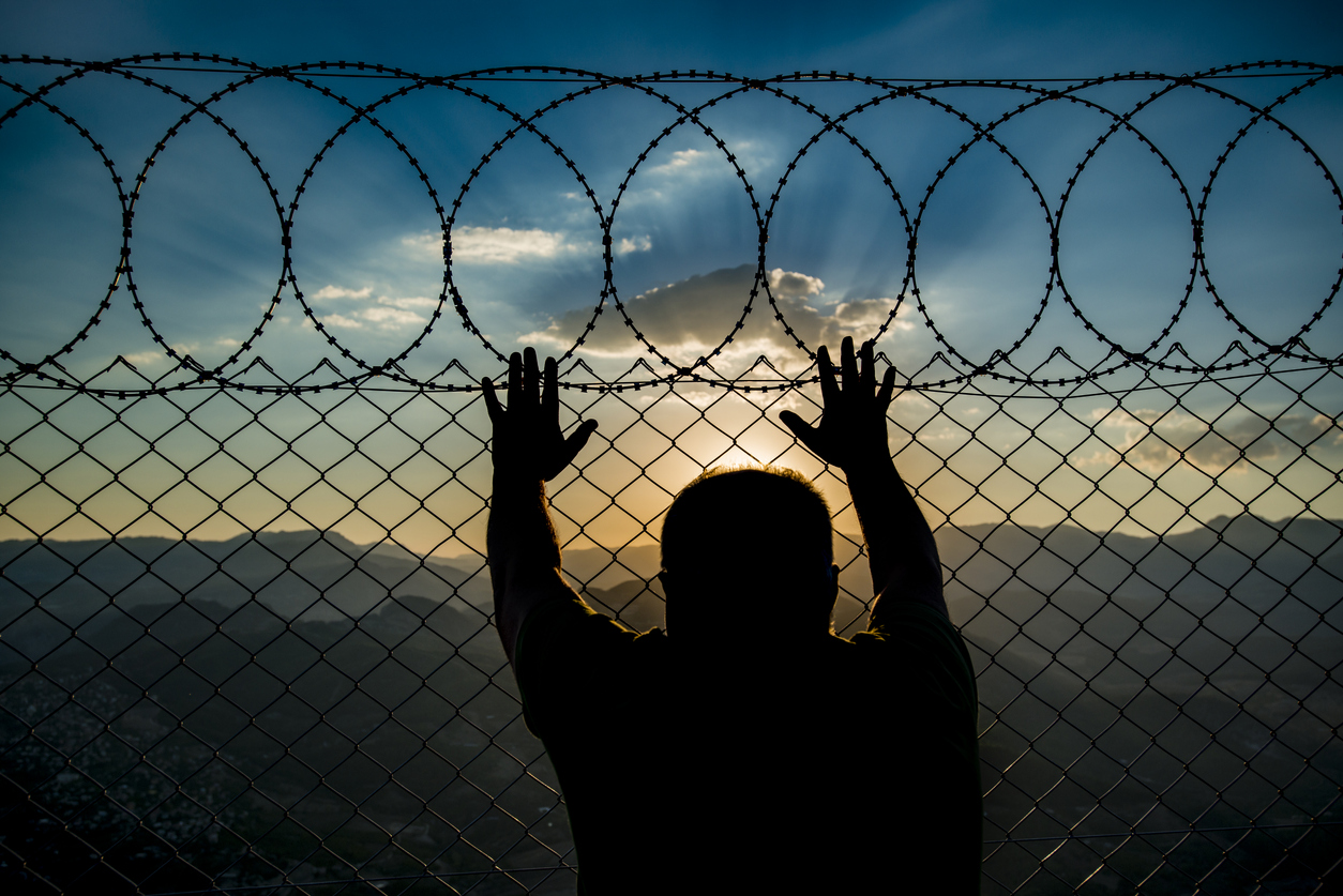 Man in jail holding the barbed wire fence while looking out